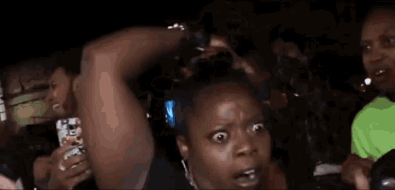 a woman is making a funny face while holding a cell phone in a crowd of people .