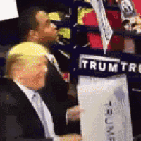 a man in a suit and tie is sitting in front of a sign that says trump .