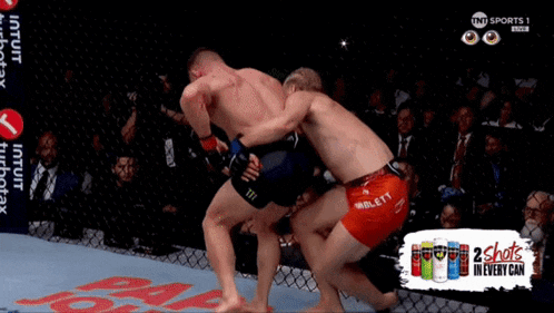 two men are fighting in a cage with an ad for 2 shots in every can behind them
