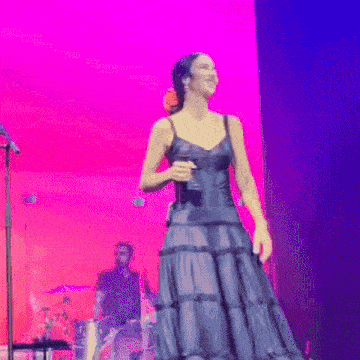 a woman in a black dress is singing into a microphone on stage