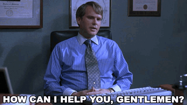 a man in a blue shirt and tie is sitting at a desk with the words how can i help you gentlemen