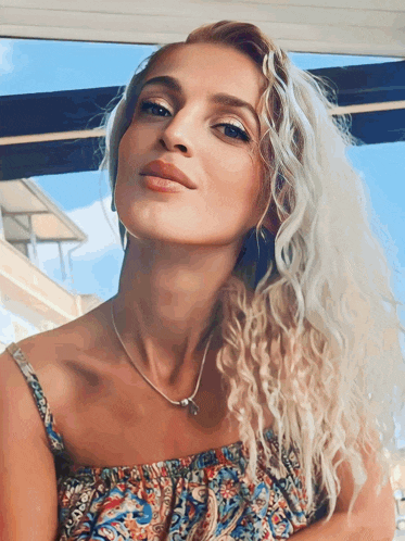 a woman with curly blonde hair wearing a necklace and earrings