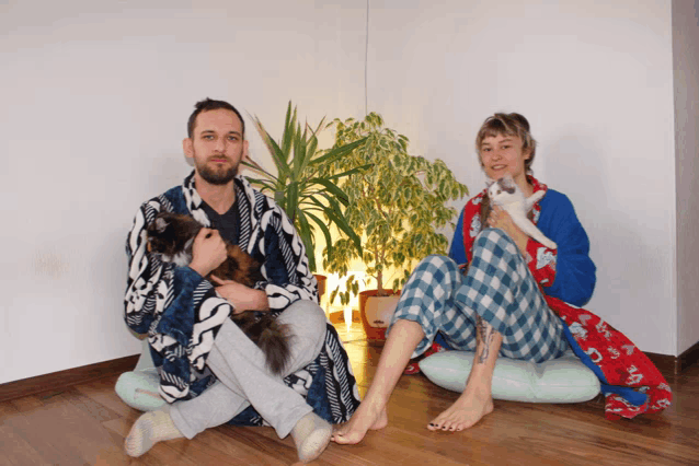 a man and a woman sit on the floor with a cat