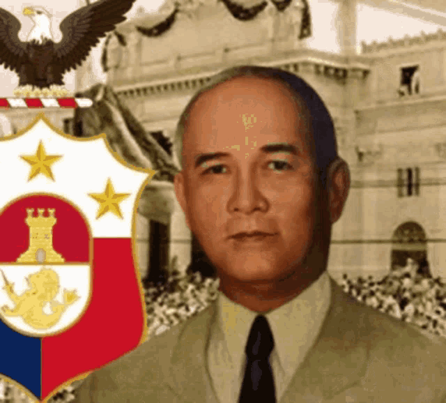 a man in a suit and tie stands in front of a coat of arms with an eagle on top