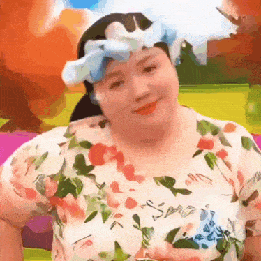a woman wearing a floral shirt and a blue bow on her head is smiling