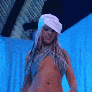 a woman is standing in front of a blue curtain wearing a white hat and no shirt .
