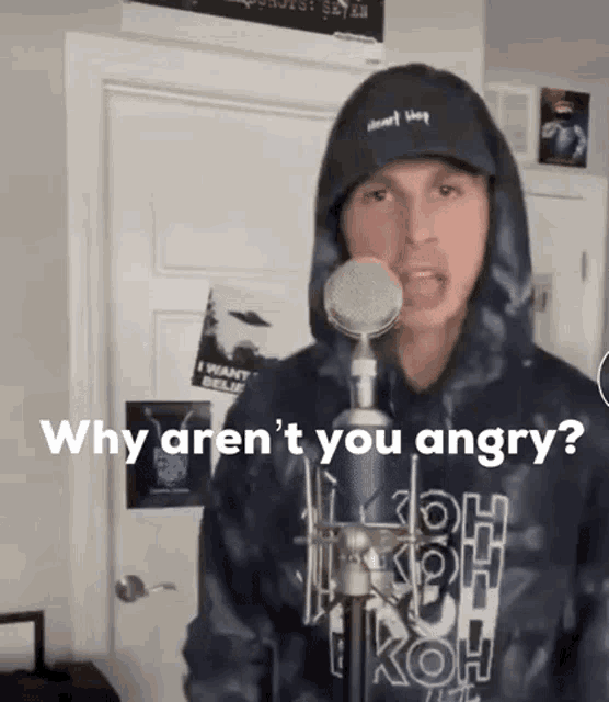 a man in a tie dye hoodie is singing into a microphone while wearing a hat .