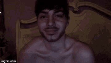 a shirtless man with a beard is sitting on a bed with his mouth open .