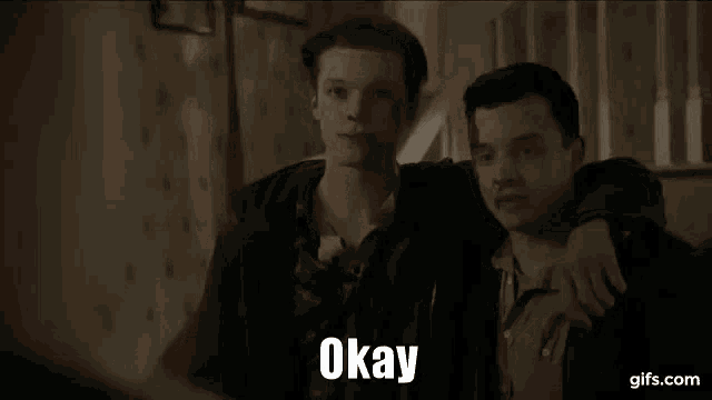 two young men are sitting next to each other in a room and one of them is saying okay .
