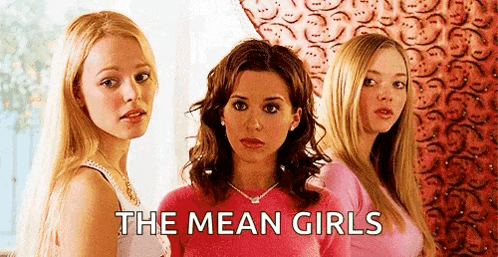 three women are standing next to each other in front of a wall with the words `` the mean girls '' written on it .