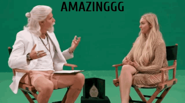 a woman sits in a director 's chair talking to a man in a white coat with amazinggg written on the bottom