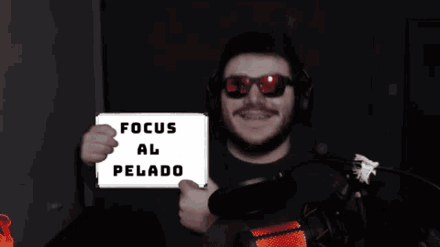 a man wearing sunglasses and headphones holds up a sign that says focus al pelado