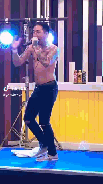 a shirtless man is singing into a microphone while dancing on stage .