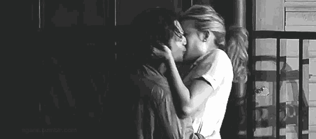 a black and white photo of a man and a woman kissing on a balcony .