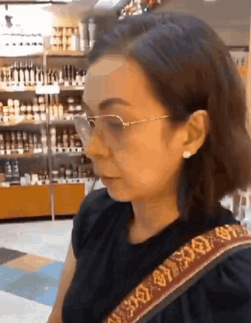 a woman wearing glasses and a black shirt is standing in front of a store shelf .