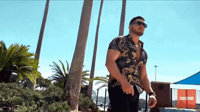 a man wearing sunglasses is standing in front of a sign that says subscribe .