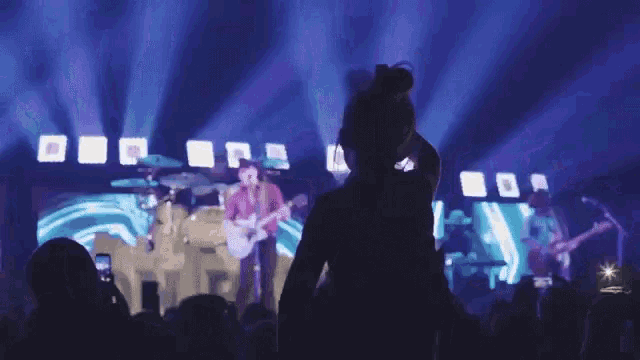 a woman stands in front of a stage watching a band play