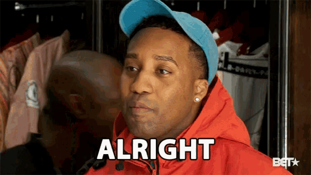 a man wearing a blue hat and a red jacket is saying alright .