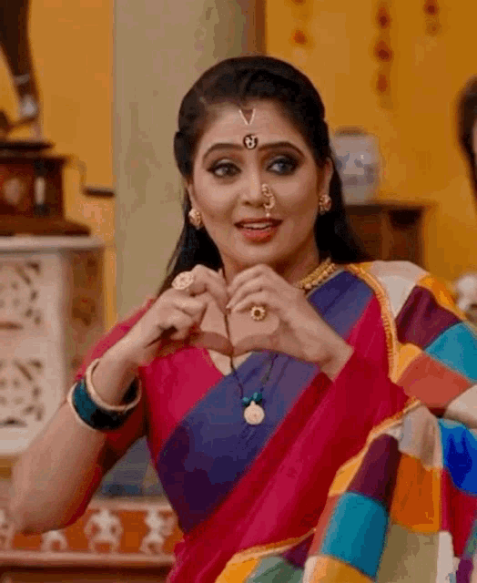 a woman in a colorful saree making a heart with her hands