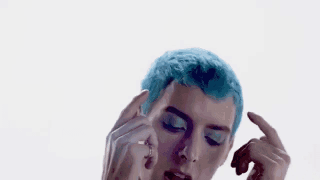 a man with blue hair is covering his ears with his hands while making a funny face .