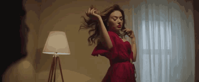 a woman in a red dress is dancing in a room with a lamp