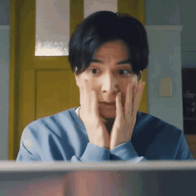 a man is looking at a computer screen with his hands on his face and making a surprised face .