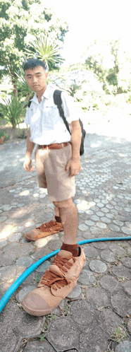 a boy wearing a backpack stands next to a hose and a pair of shoes