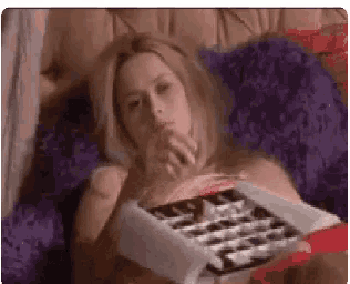 a woman is laying on a bed with a box of chocolates in her hand .