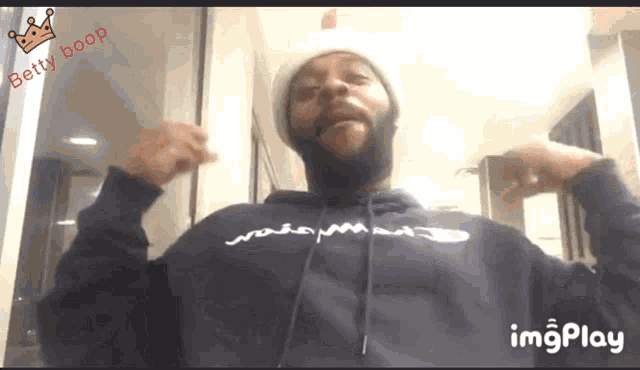 a man with a beard wearing a blue hoodie and a white hat with betty boop written on the top