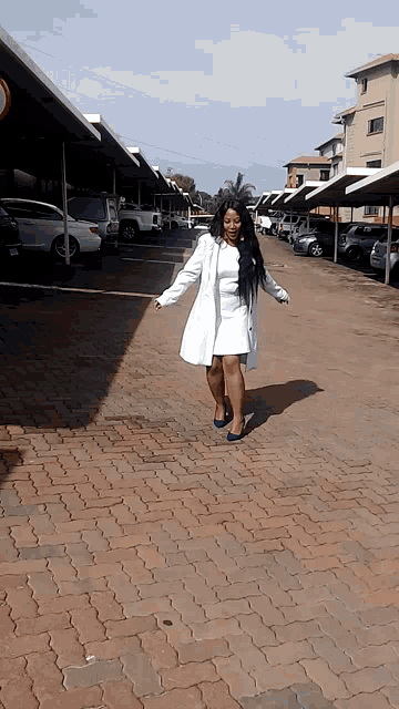 a woman in a white coat stands on a brick sidewalk