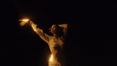 a woman in a white top is dancing in the dark while holding a fire in her hands .