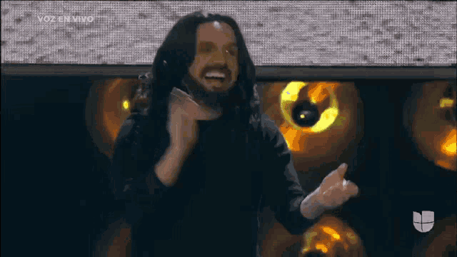 a man with long hair and a beard is standing on a stage with his arms outstretched .