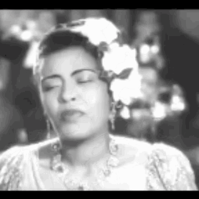a black and white photo of a woman with her eyes closed and a flower in her hair