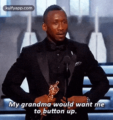a man in a suit and bow tie is holding an oscar trophy and saying `` my grandma would want me to button up ''