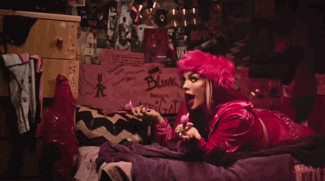 a woman in a pink outfit is laying on a bed with a poster that says blink on it