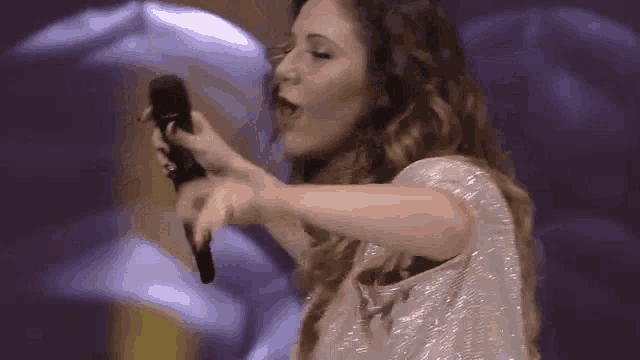 a woman in a white dress is singing into a microphone on a stage .