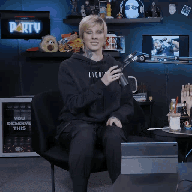 a woman wearing a black liquid hoodie sits in a chair