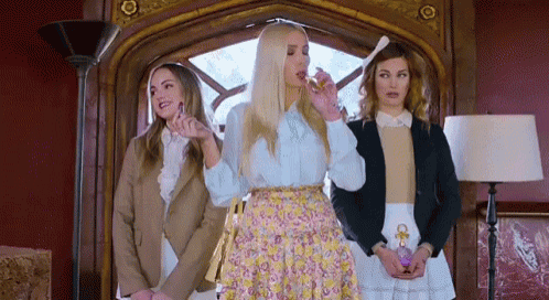three women are standing next to each other and one of them is holding a bottle of perfume