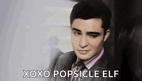 a man in a suit and tie is making a face and saying `` xoxo popsicle elf '' .