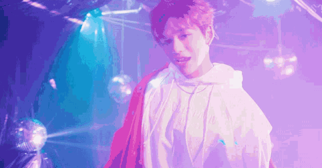 a man in a white hoodie is standing in front of a disco ball