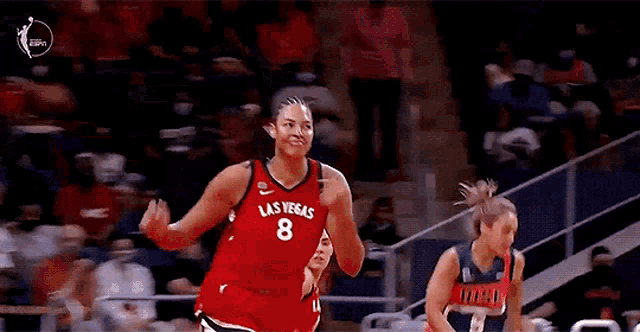 a female basketball player wearing a red jersey with the number 8 on it is jumping in the air during a game .