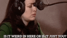 a woman wearing headphones is talking into a microphone and asking is it weird in here or is it just you ?