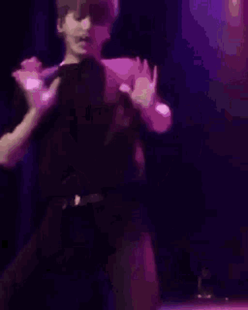 a man in a black shirt and yellow pants is dancing on a stage in front of a purple background .