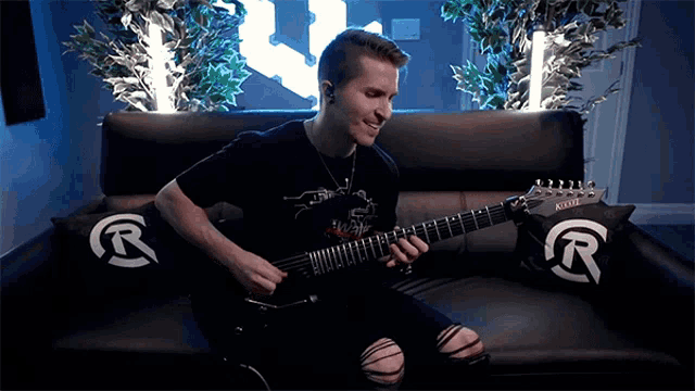 a man is sitting on a couch playing a guitar with the letter r on the back
