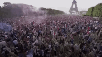 a large crowd of people are gathered in a park in front of the eiffel tower .