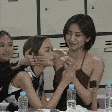 a woman kisses another woman on the cheek in front of a table with water bottles
