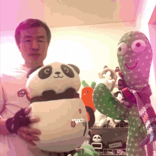 a man is holding a stuffed panda and a stuffed cactus with the word yuxk on it