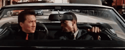 a man in a suit and tie is driving a car with another man in the back seat