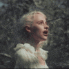 a woman in a white dress is standing in a forest looking up at the sky .