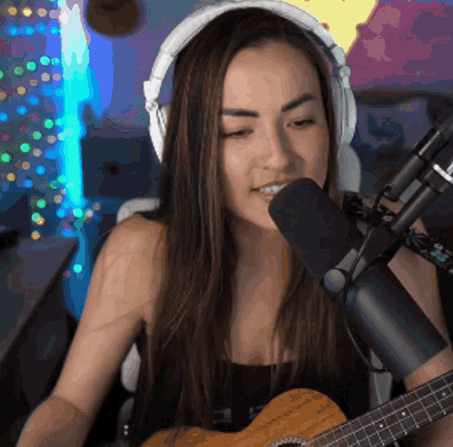 a woman wearing headphones singing into a microphone while holding a guitar
